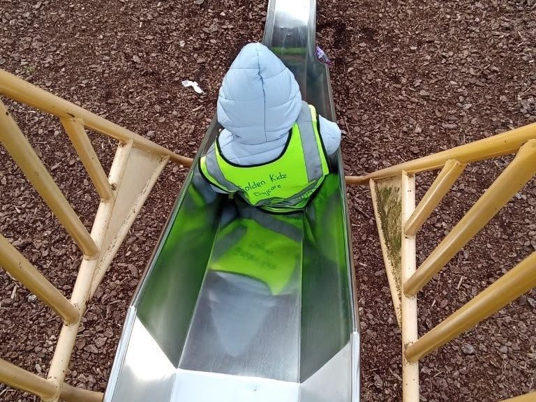 A child in a Golden Kidz Daycare high-visibility vest at the top of a slide during an outing to a Birmingham park